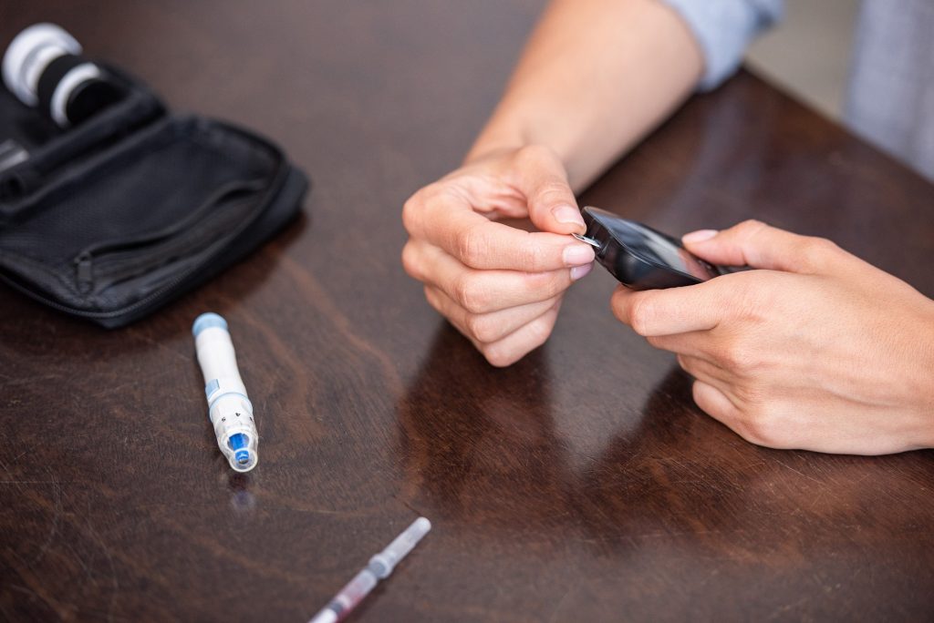 selective focus of woman holding glucose monitor while doing blood test at home